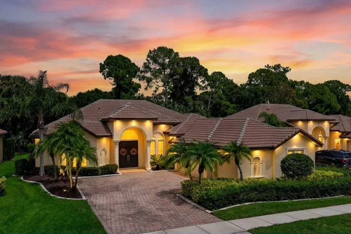 Tile roof, arched entryway, paver driveway, mature landscaping.