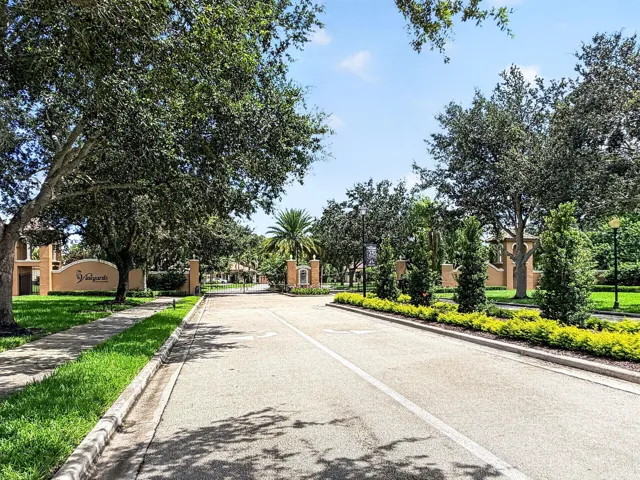 Roadway entry with a landscaped median, mature trees, and decorative signage