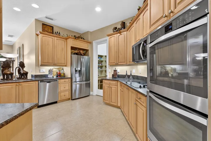 Kitchen featuring wood cabinetry, stainless steel appliances, dark stone countertops, and tile flooring