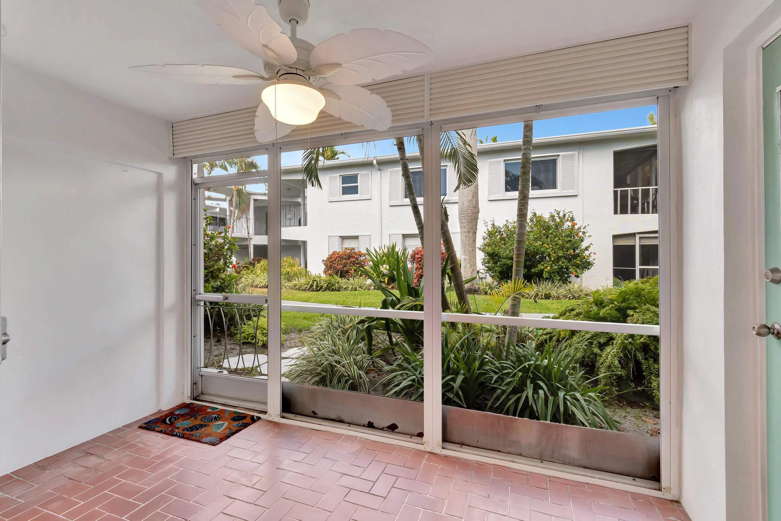 Screened enclosure with terracotta tile flooring, ceiling fan with integrated lighting, and white panel walls