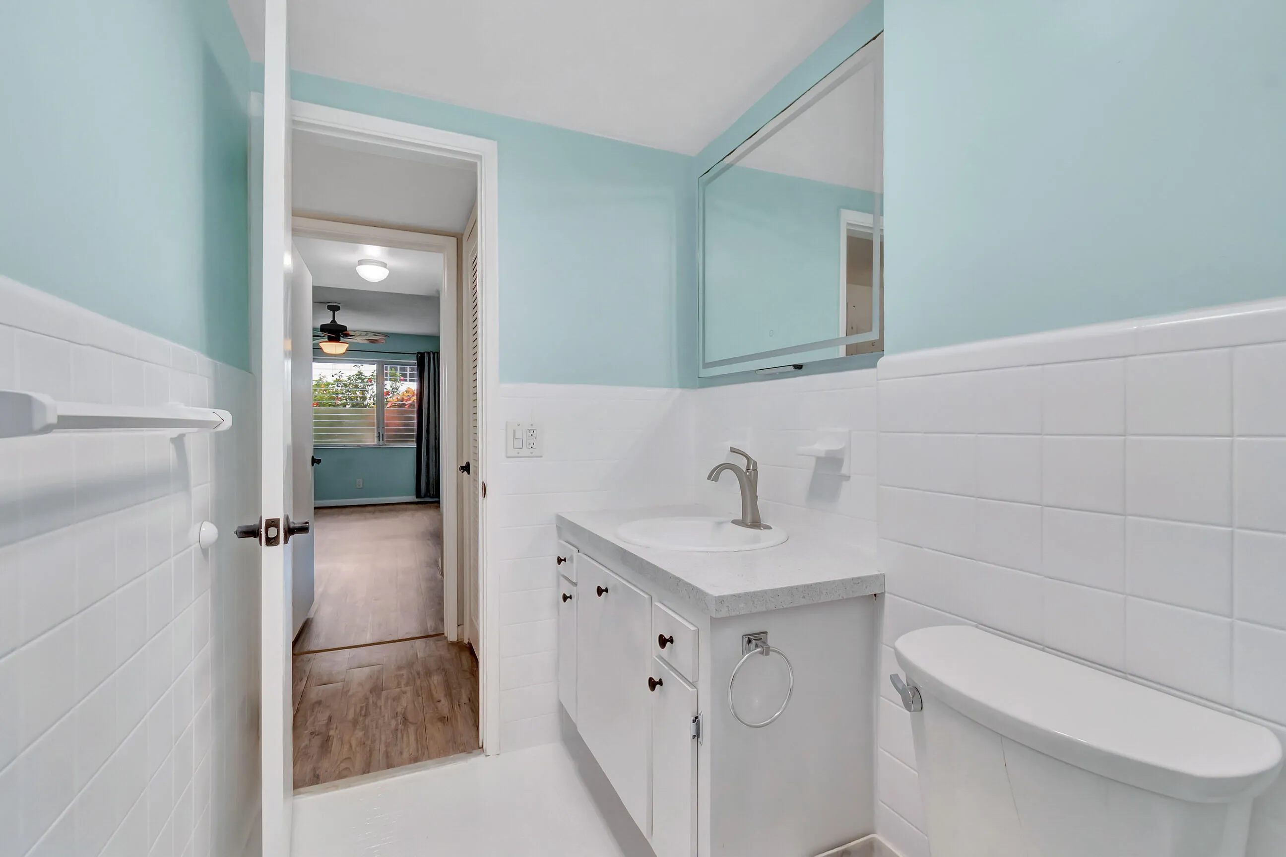 Bathroom featuring a single vanity with a white countertop, an integrated sink, a medicine cabinet, and white tile wainscoting