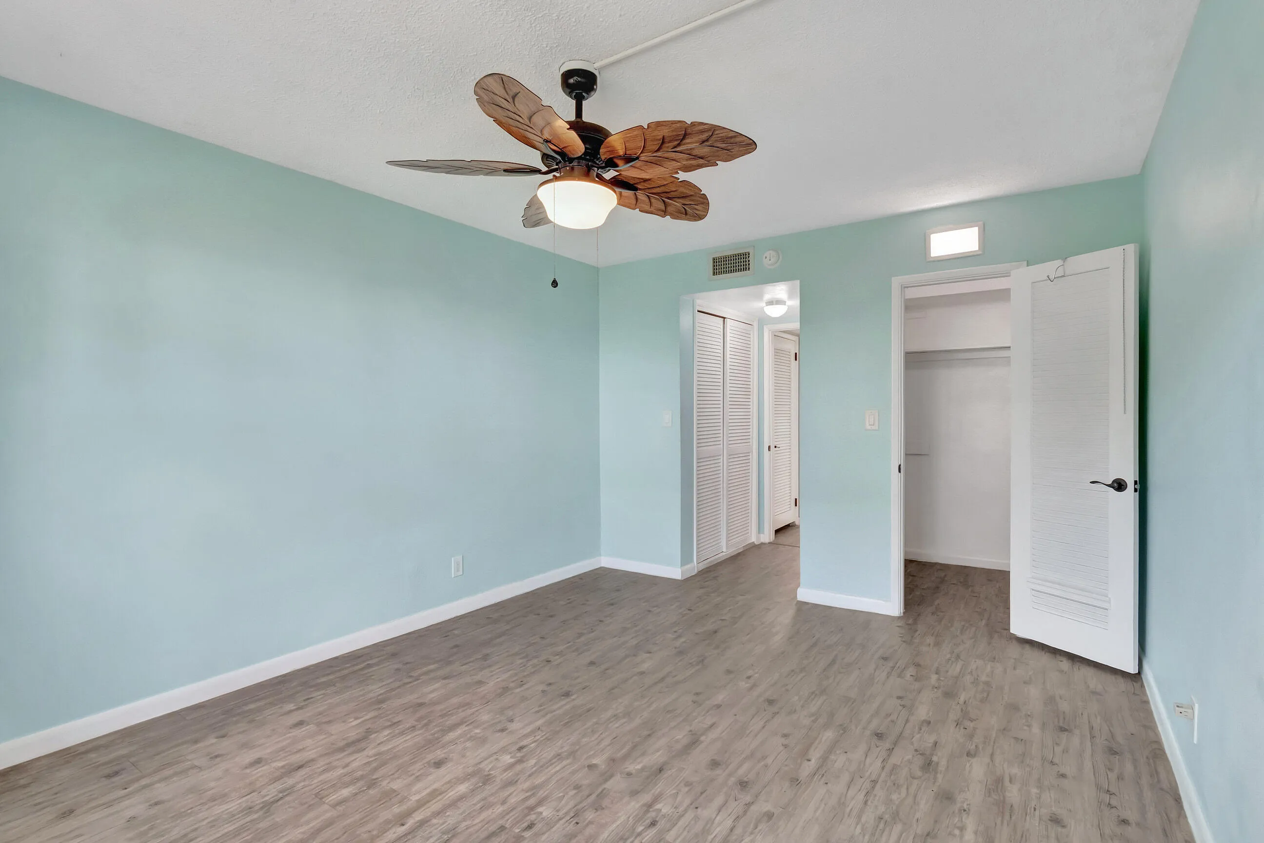 Room featuring wood-finish flooring, a ceiling fan with integrated lighting, and a closet with louvered bifold doors