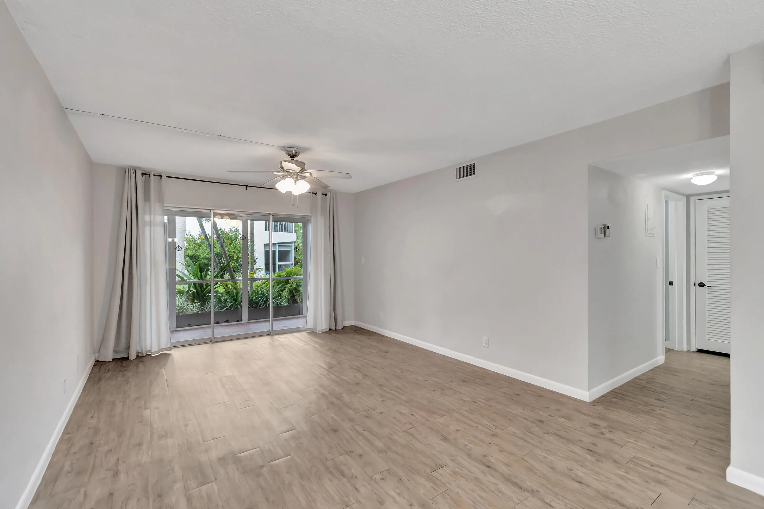 Wood-finish flooring throughout, sliding glass doors to outdoor space, ceiling fan with integrated lighting, and neutral wall color