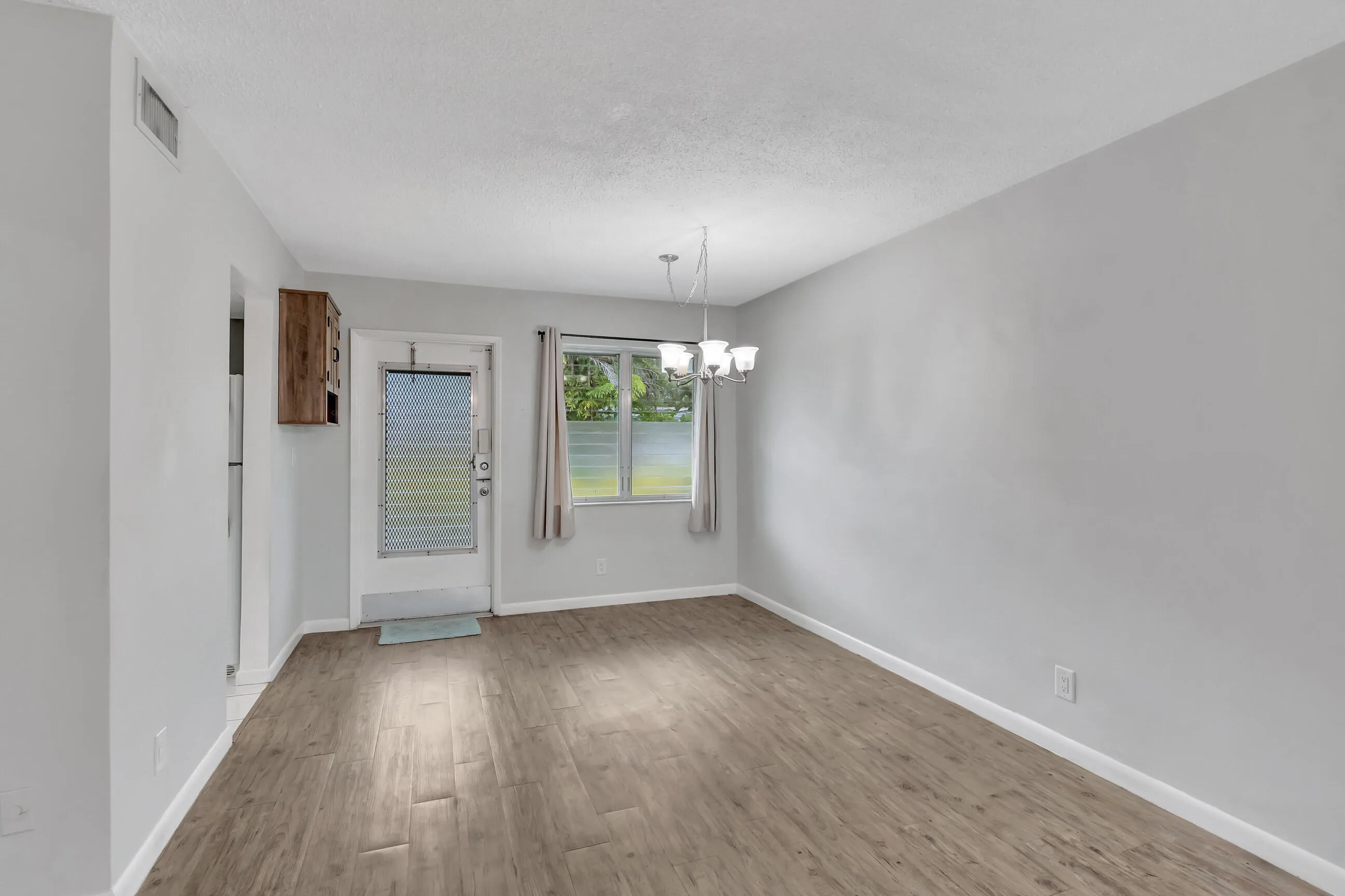 Wood-finish flooring, light gray walls, built-in wooden cabinet, and window with exterior landscaping