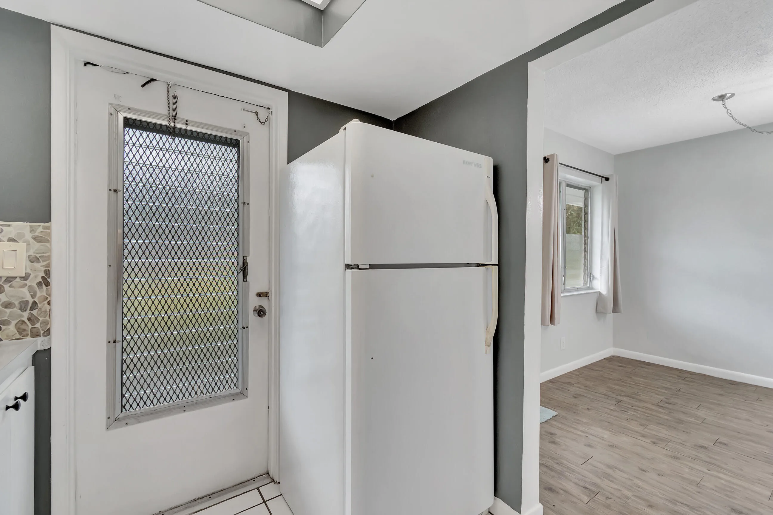 Kitchen featuring a mosaic tile backsplash, white cabinetry with dark hardware, and an attached refrigerator