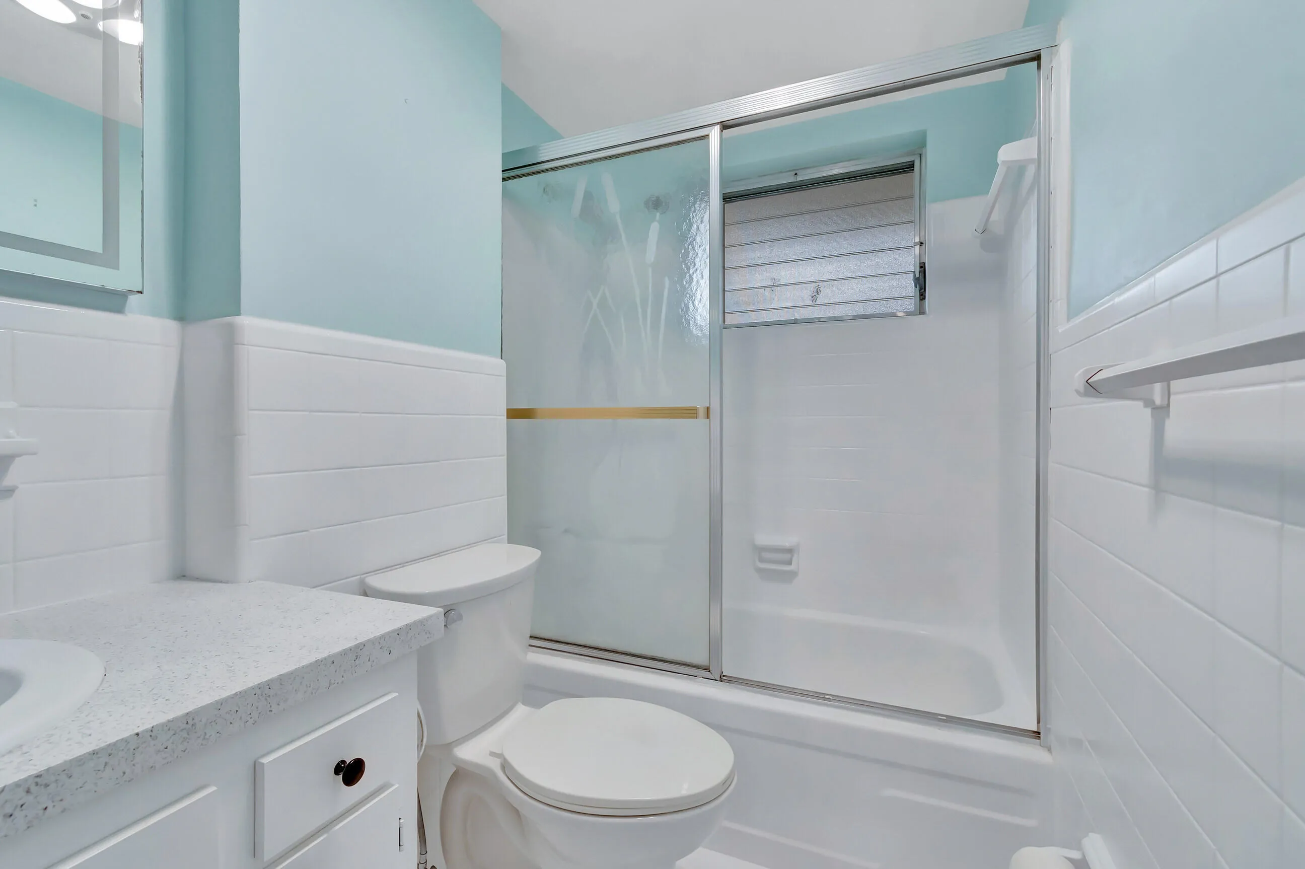 Bathroom featuring a bathtub with sliding glass doors, a window, a white vanity with an integrated sink, and white wall tiling