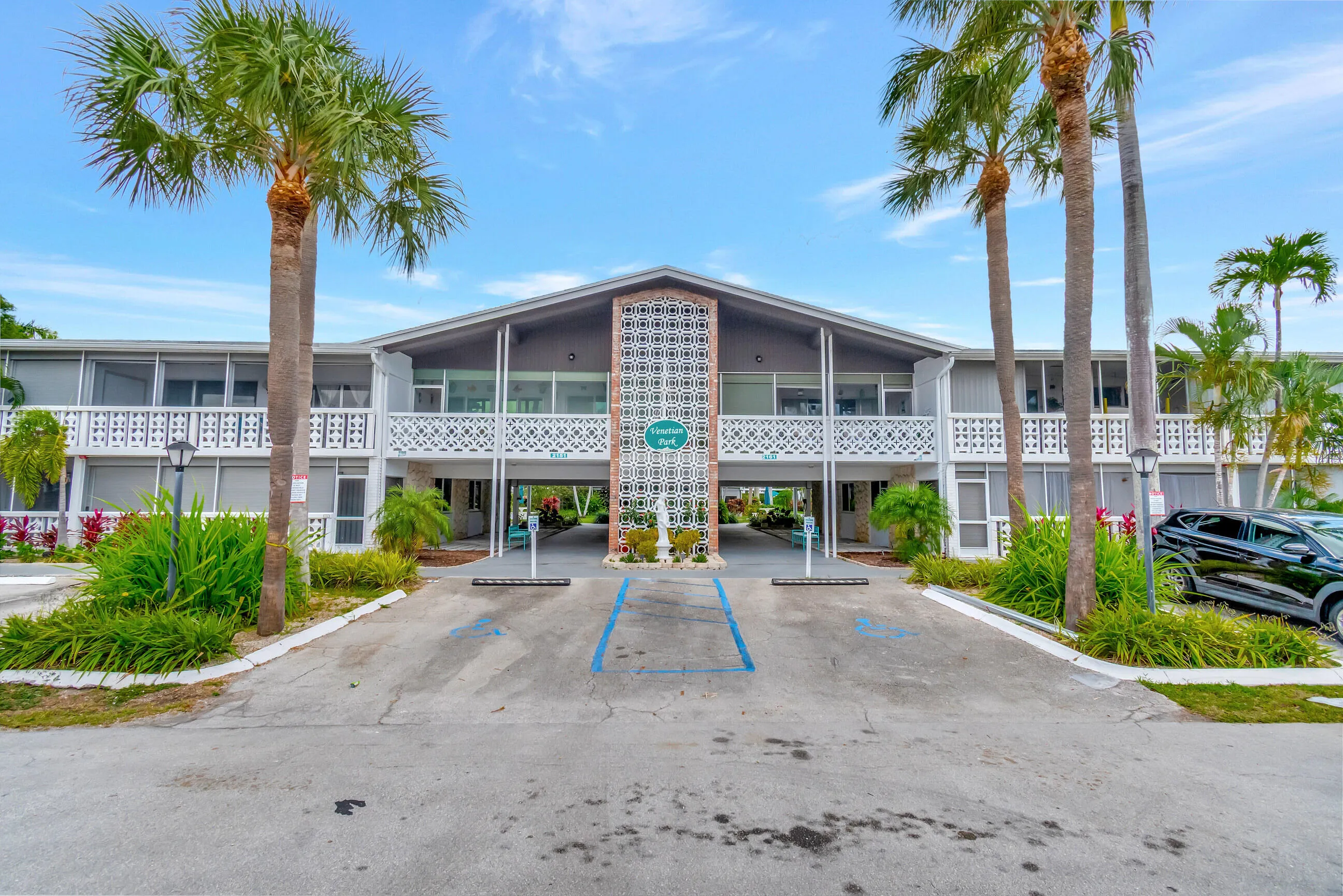 Two-story residential building with screened lanais, decorative white balcony railings, and a central breezeway entrance