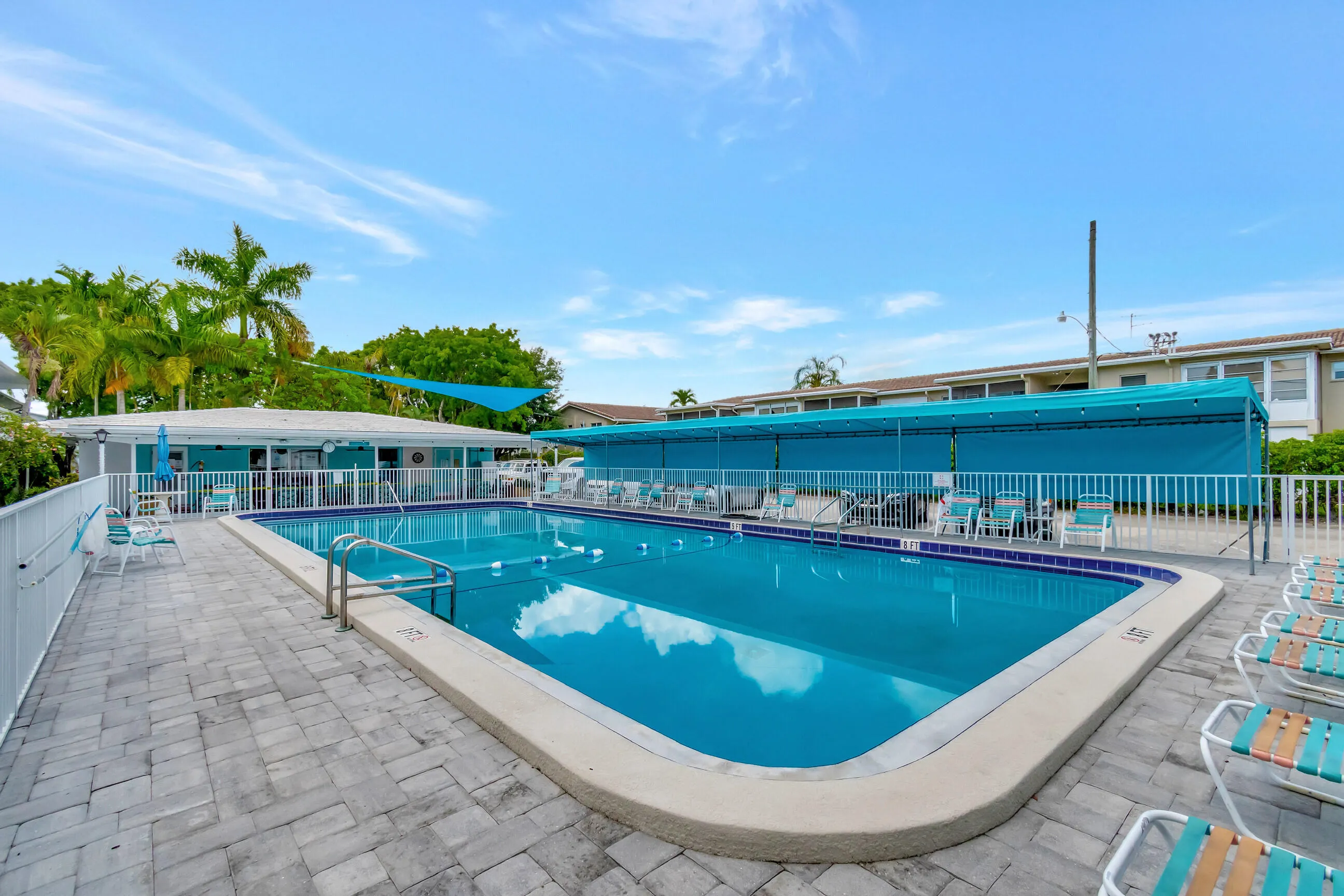 Rectangular swimming pool with integrated steps, surrounded by paver patio surfacing, a poolside building, and a shaded outdoor area