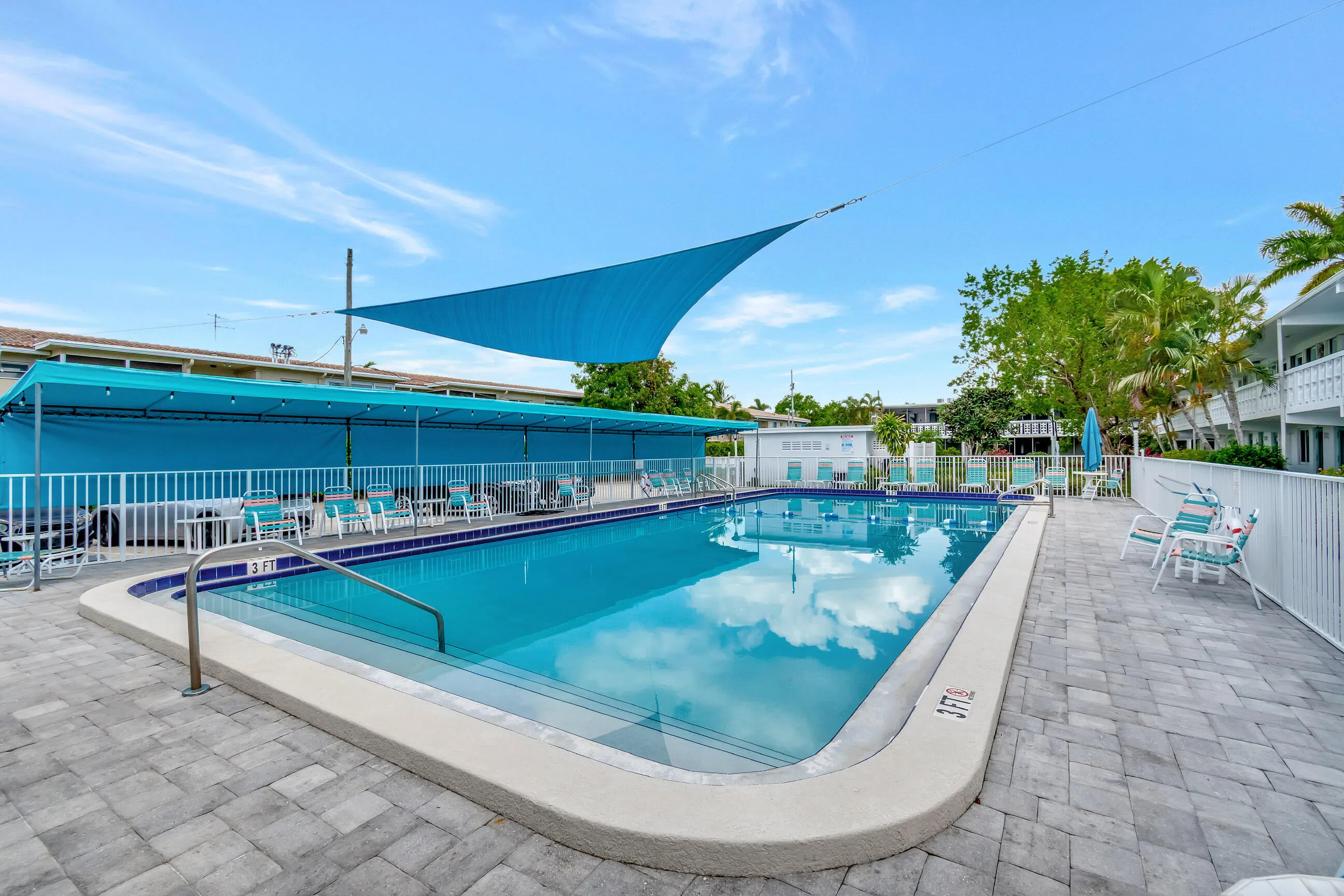 Resort-style swimming pool with integrated steps, surrounded by a paver patio and a white perimeter fence