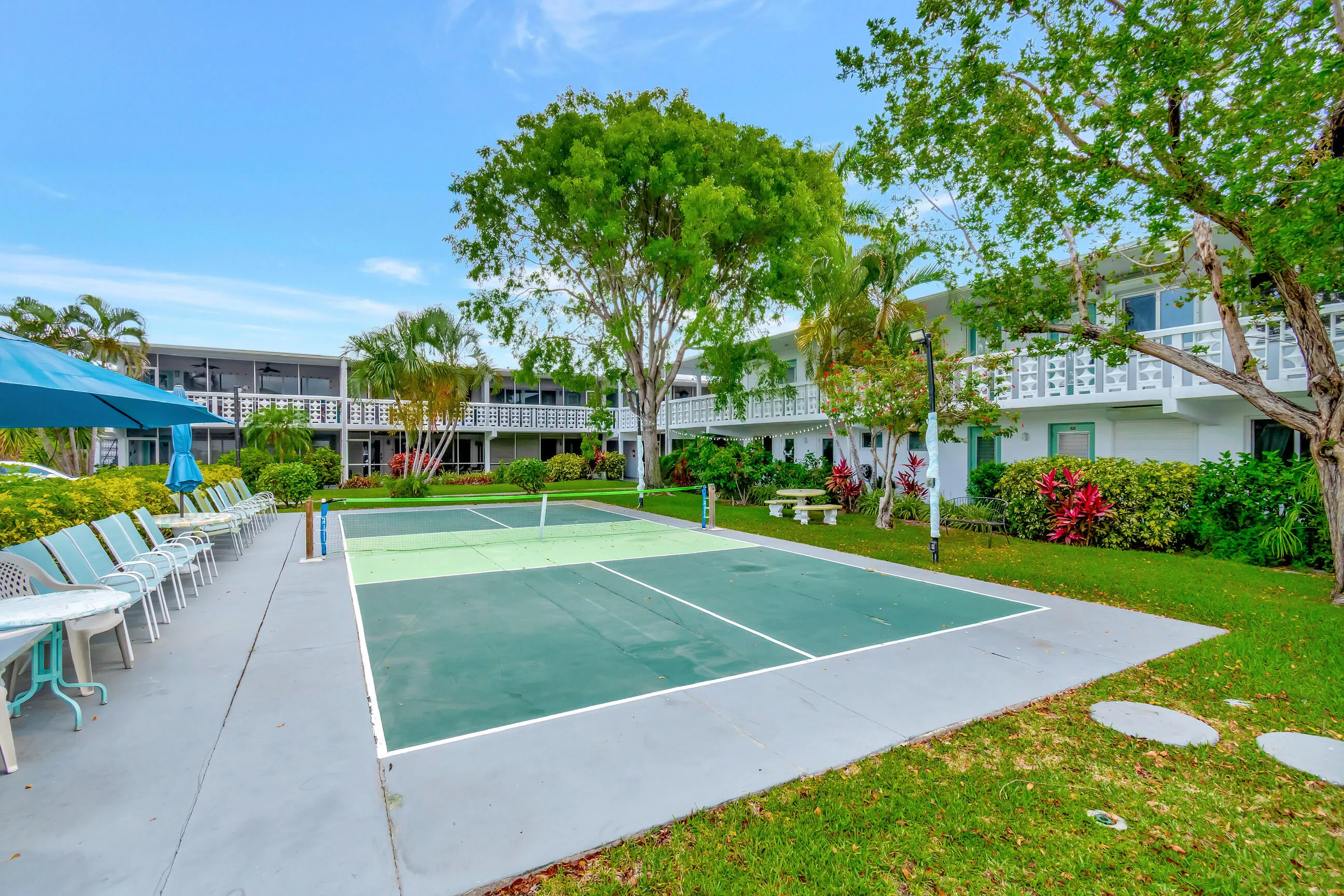 Outdoor court for recreation, extensive hardscaping, mature trees, manicured lawns, and multi-story white buildings with balconies