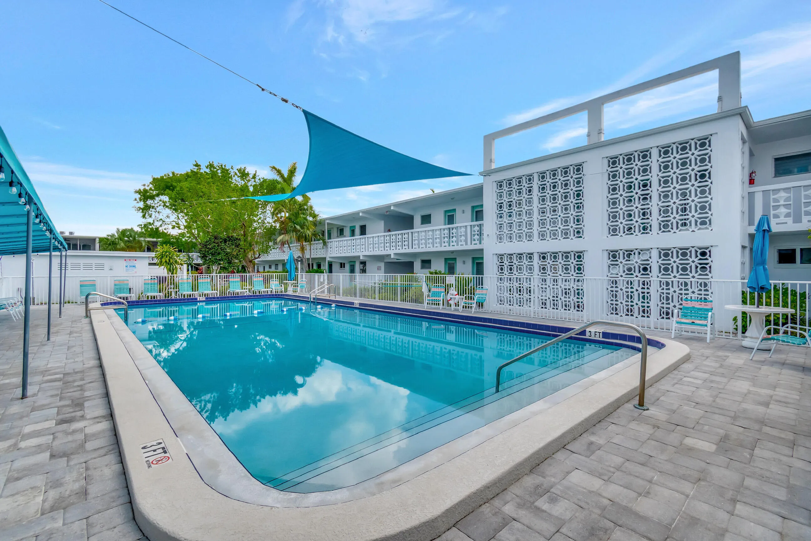 Outdoor swimming pool with integrated steps, surrounded by a paver patio and security fencing