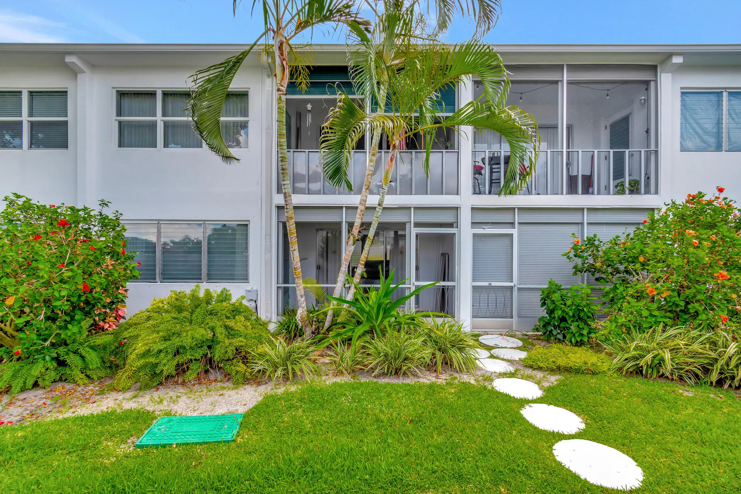 White stucco exterior with multiple windows, lush landscaping, a stone paver pathway, and two screened-in balconies