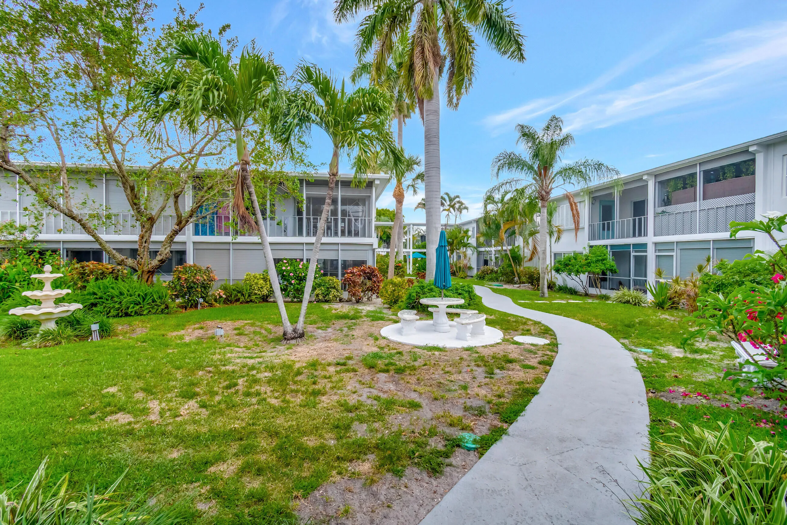 Lush landscaping featuring mature palm trees, a tiered fountain, and a meandering paver pathway