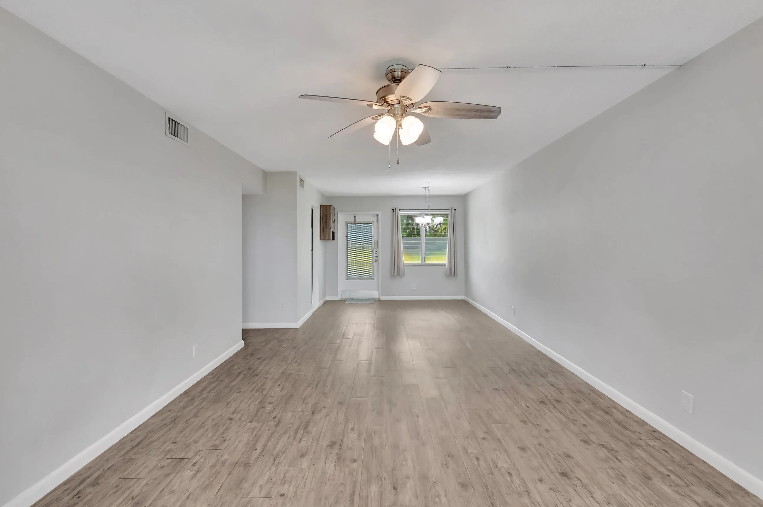 Expansive interior with wood-finish flooring, light gray walls, a ceiling fan, and a glass-paneled exterior door