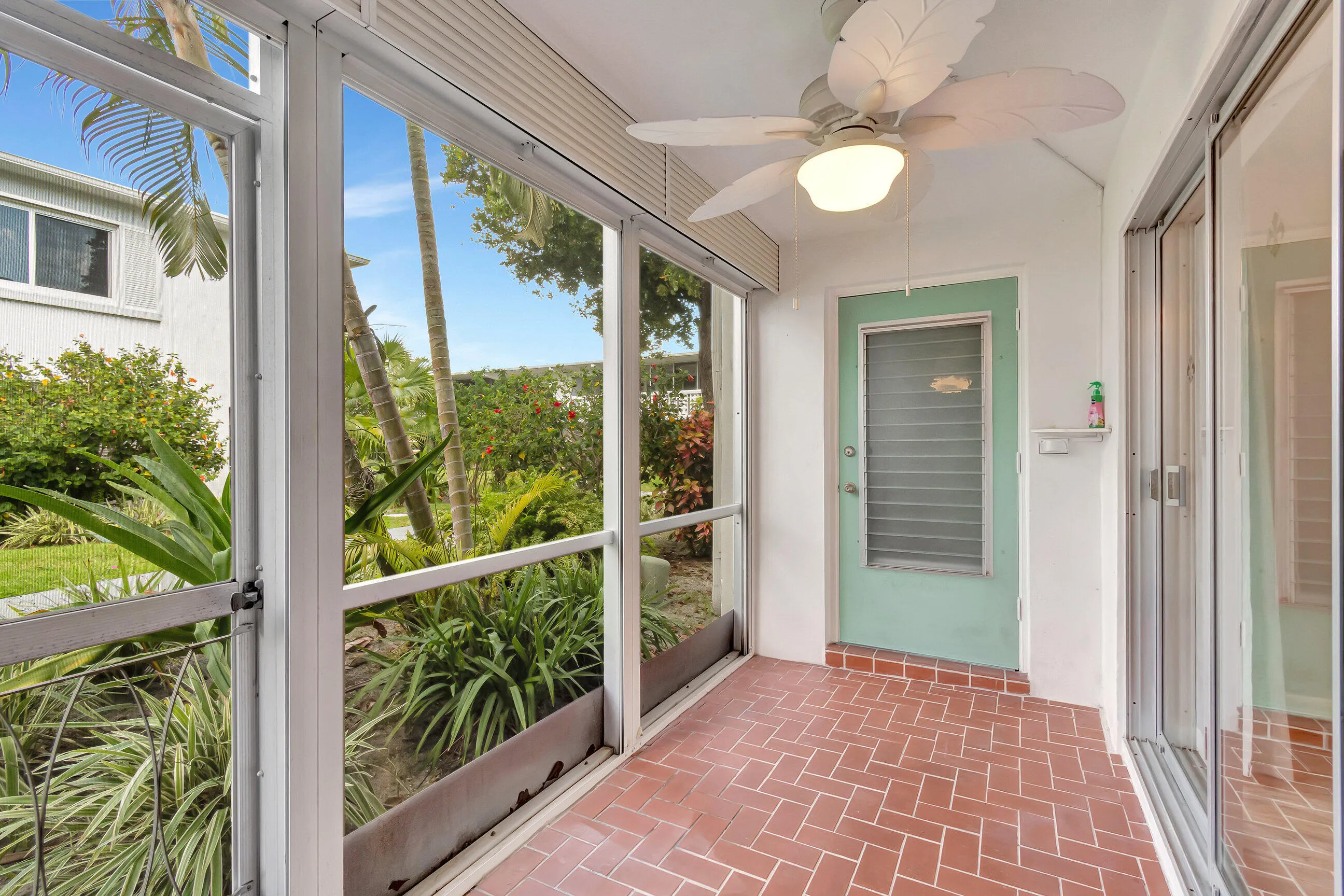 Screened patio featuring herringbone-patterned brick-finish flooring, a ceiling fan with integrated lighting, and a paneled door