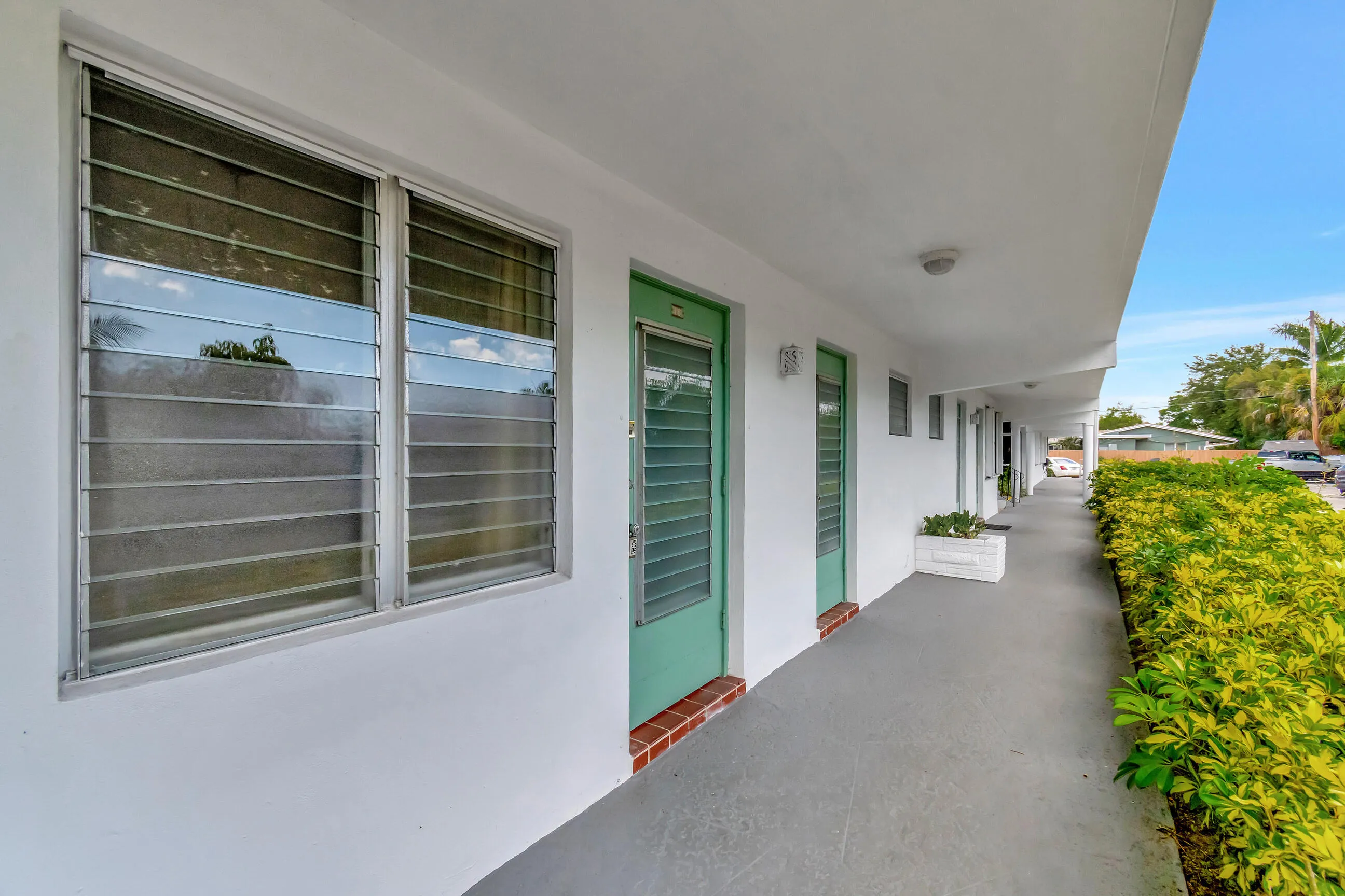 White exterior with green entry doors, louvered windows, and a paved walkway