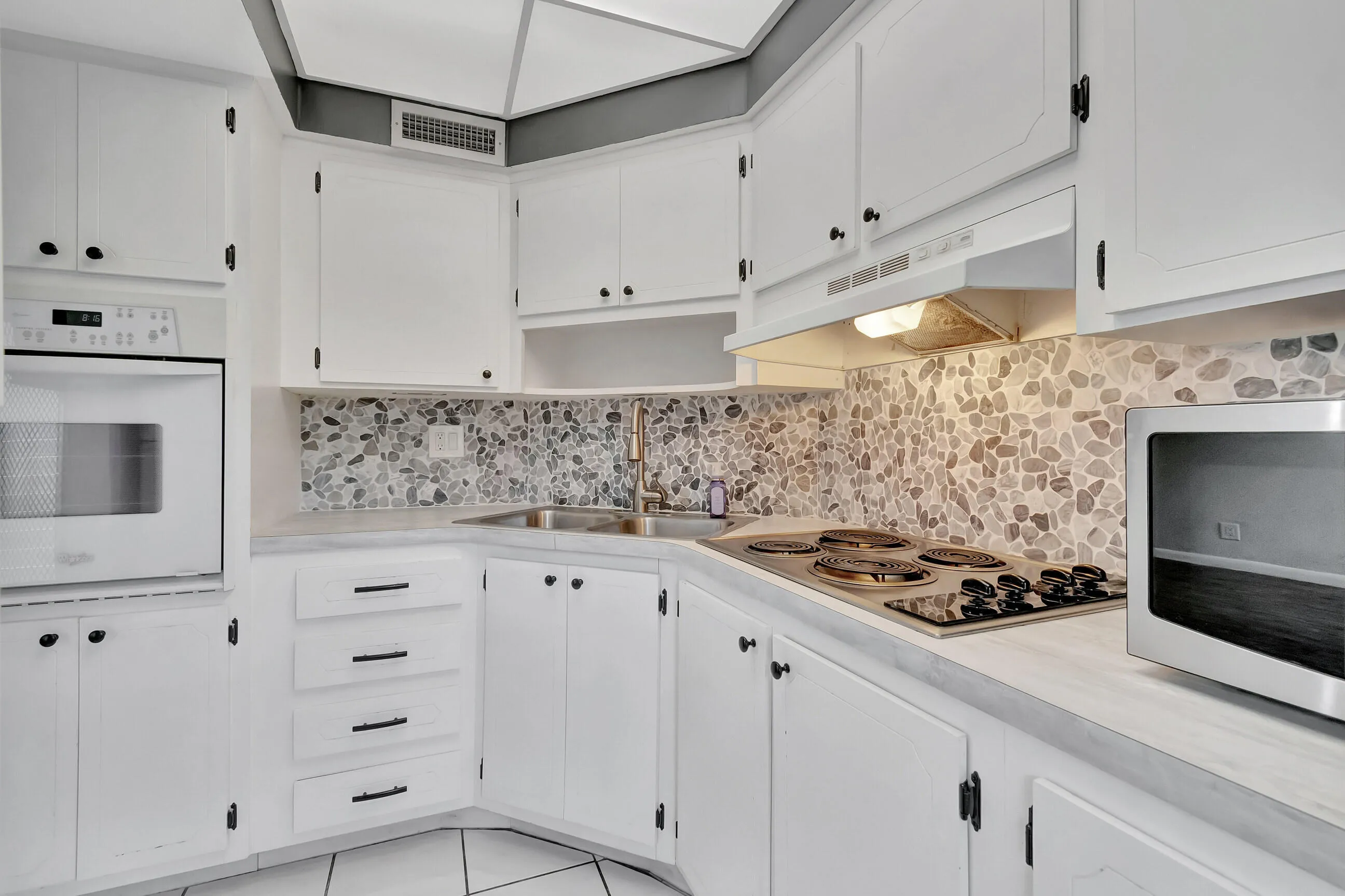Kitchen featuring white cabinetry, pebble tile backsplash, built-in wall oven, and a cooktop