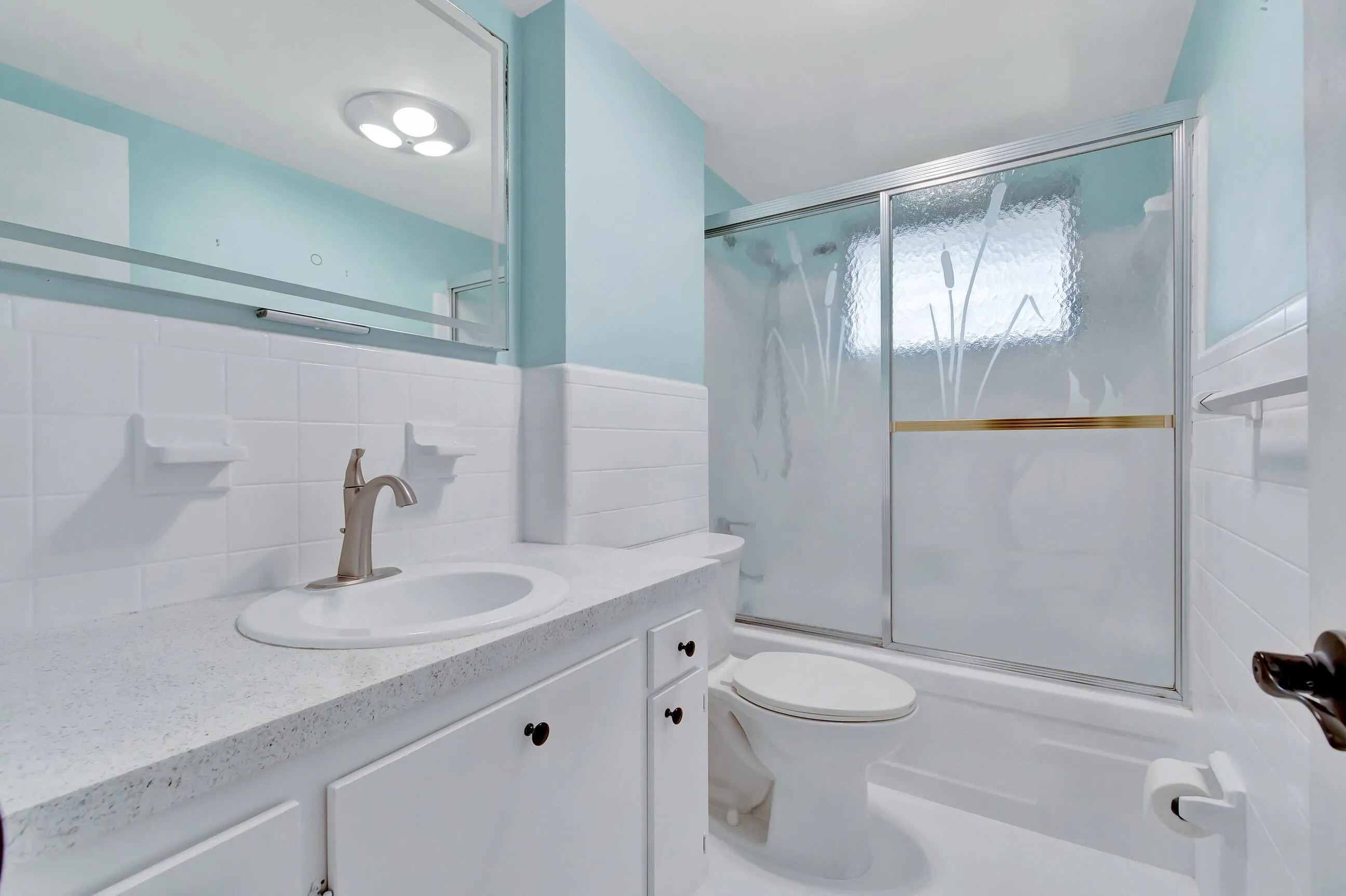 Bathroom featuring a white vanity with integrated sink, brushed nickel faucet, and a sliding glass shower enclosure with frosted accents