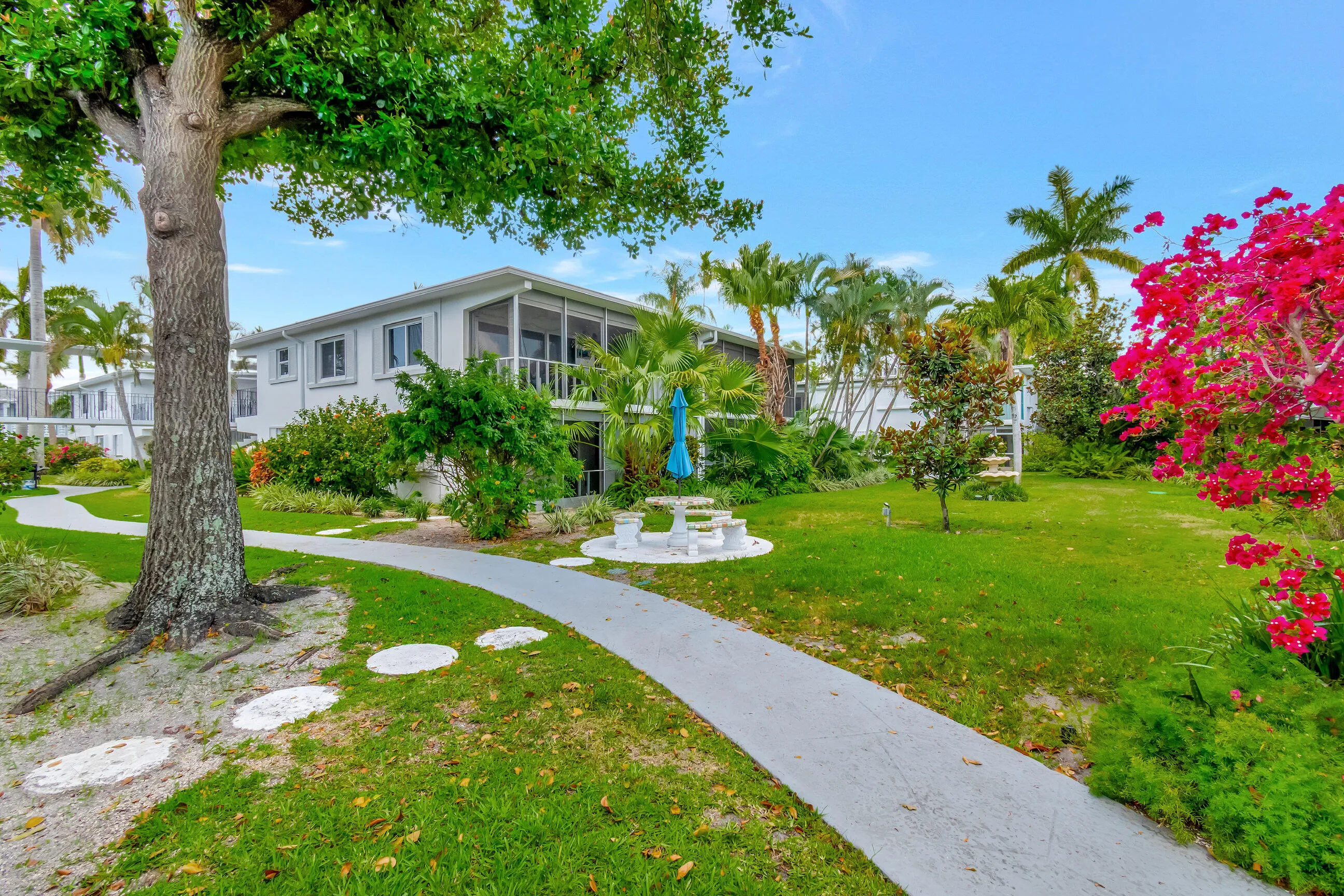 Expansive green space featuring a concrete pathway, established trees, and vibrant bougainvillea