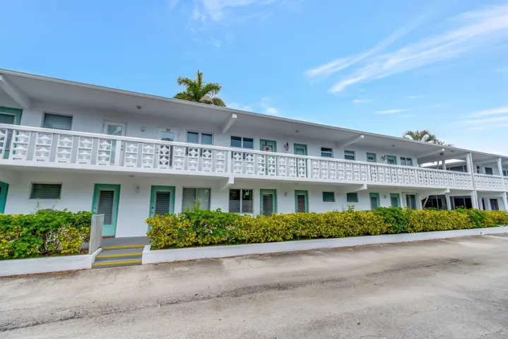 Multi-story building featuring white exterior, patterned balcony railings, and teal-framed entryways