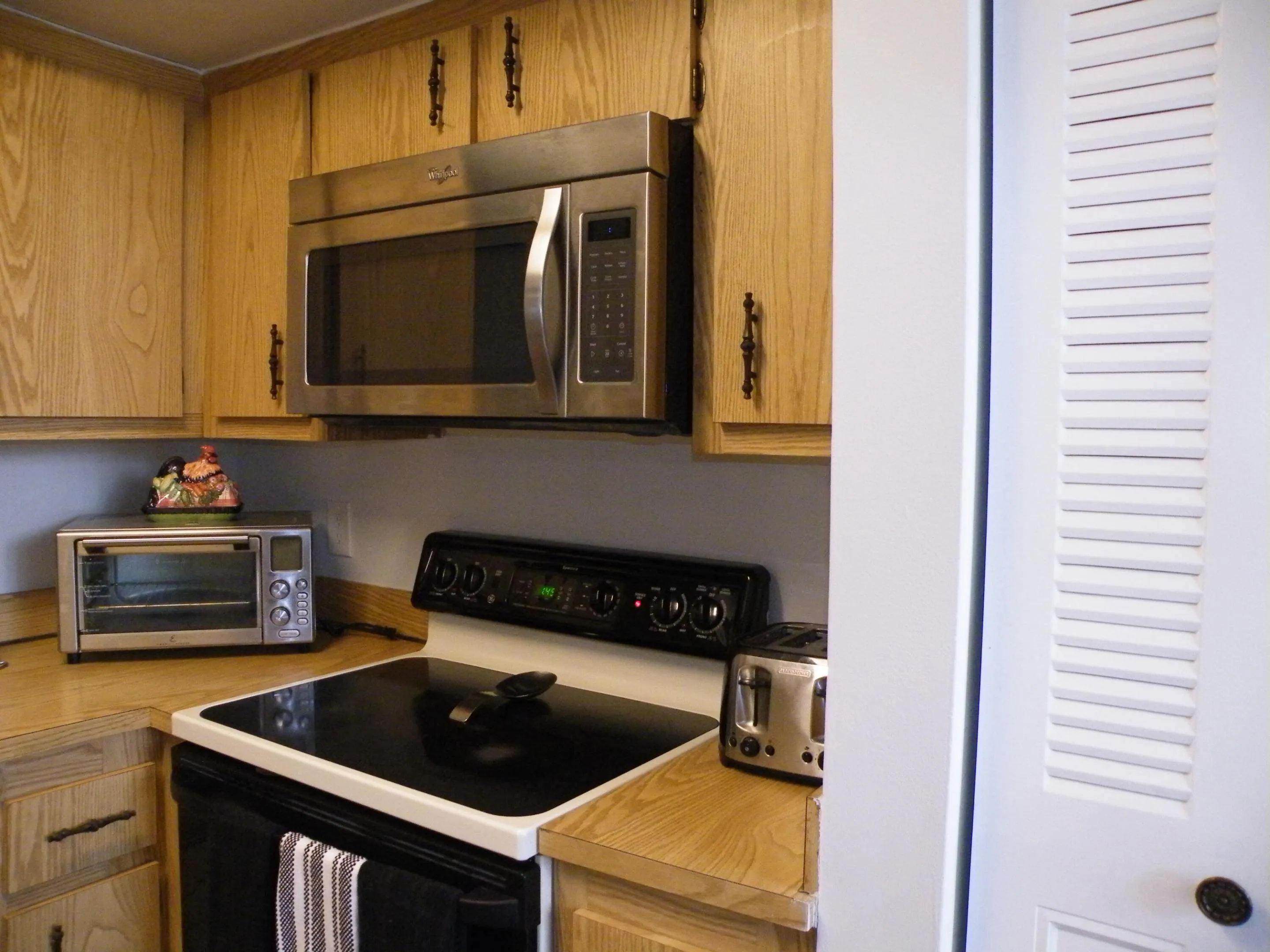 Wood-finish cabinetry with dark hardware, stainless steel microwave, black electric range with a smooth cooktop, and wood-finish countertops