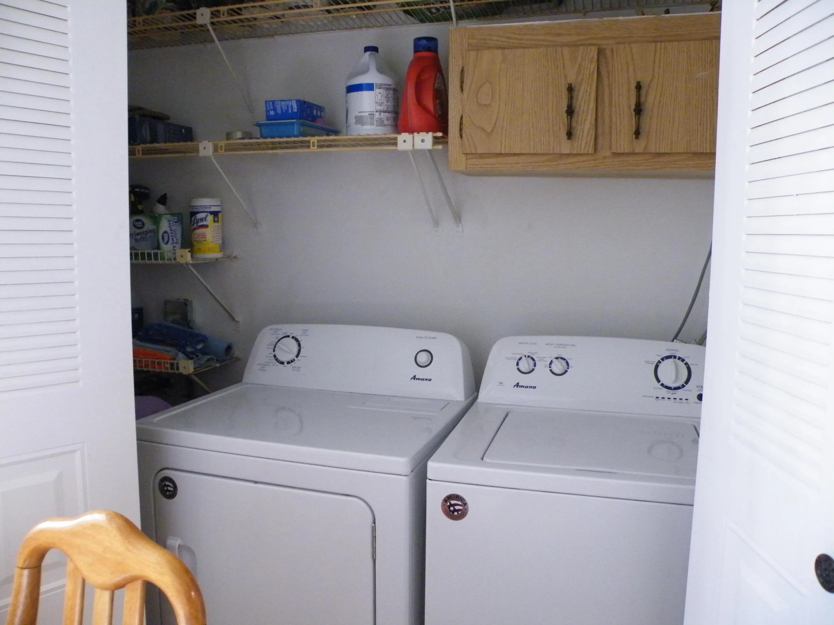 Built-in laundry closet with louvered doors, overhead cabinetry, and wire shelving