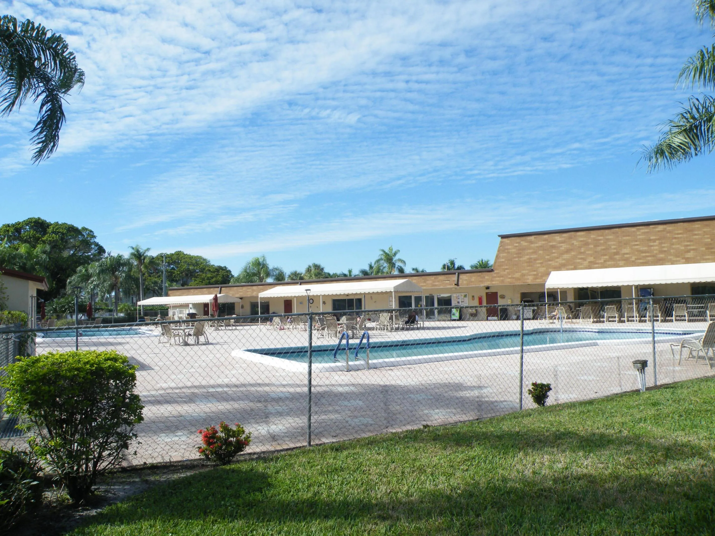 Resort-style pool area featuring a perimeter fence, surrounding patio, and adjacent buildings with awnings