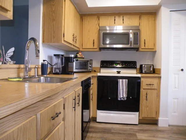 Wood-finish cabinetry, stainless steel sink, stainless steel microwave, black and white range, wood-finish countertops