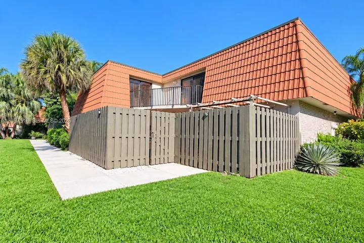 Exterior featuring a terra cotta tile mansard roof, upper-level balcony with metal railing, cedar-style privacy fencing, and concrete walkway