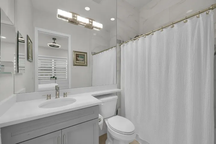 Vanity with integrated sink, modern brushed nickel faucet, large wall mirror, contemporary light fixture, and tiled shower surround