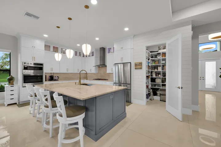 Gourmet kitchen featuring a large central island with seating, stainless steel appliances, extensive white cabinetry, and a walk-in pantry with built-in shelving