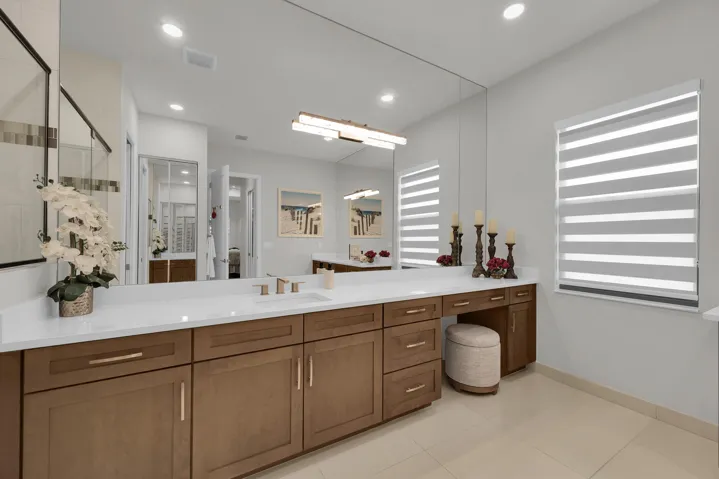 Expansive vanity with a white countertop, dual undermount sinks, wood-finish cabinetry, and full-wall mirror
