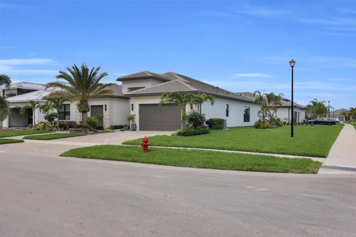 Contemporary stucco exterior with a tiled roof, two-car garage, paver driveway, and manicured lawn