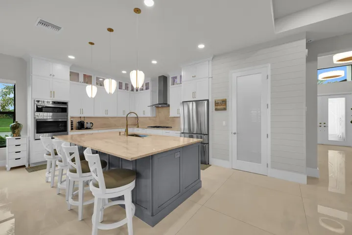 Gourmet kitchen featuring a large central island with seating, stainless steel appliances, white cabinetry with upper glass-front accents, and pendant lighting