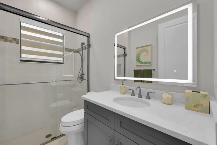 Walk-in shower with clear glass enclosure, gray vanity cabinet with white countertop, integrated sink, and illuminated mirror
