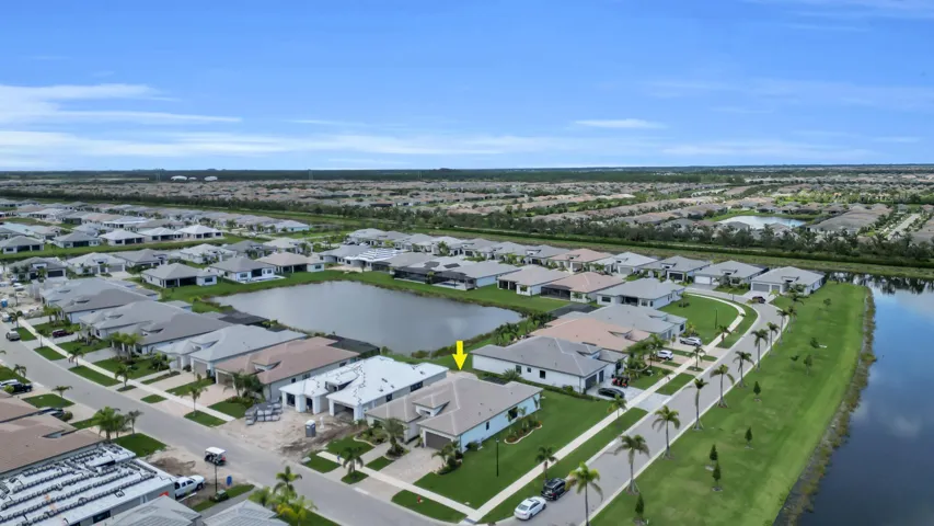 Aerial perspective of a neighborhood featuring a central pond, manicured lawns, and well-maintained roadways