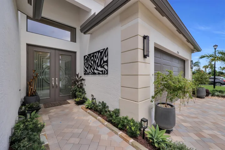 Paver driveway and walkway leading to a double-door entry with decorative glass inserts and a transom window