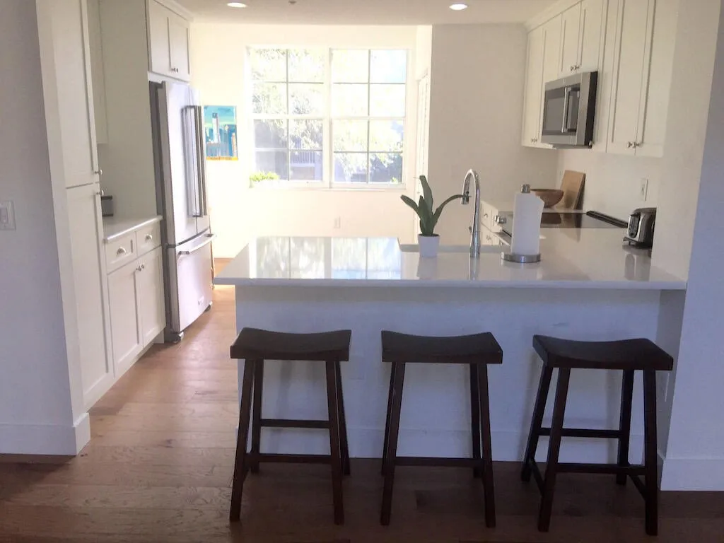Kitchen featuring white cabinetry, stainless steel appliances, a white countertop island, and wood-finish flooring