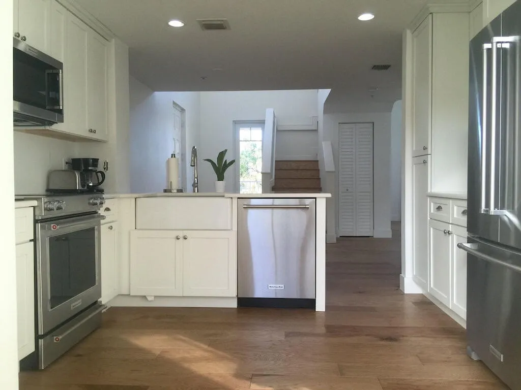 Kitchen featuring white cabinetry, stainless steel appliances, a farmhouse sink, and wood-finish flooring