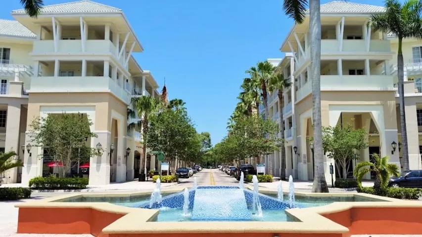 Street-level view featuring a multi-story building with multiple balconies, a tiled fountain, and mature palm trees