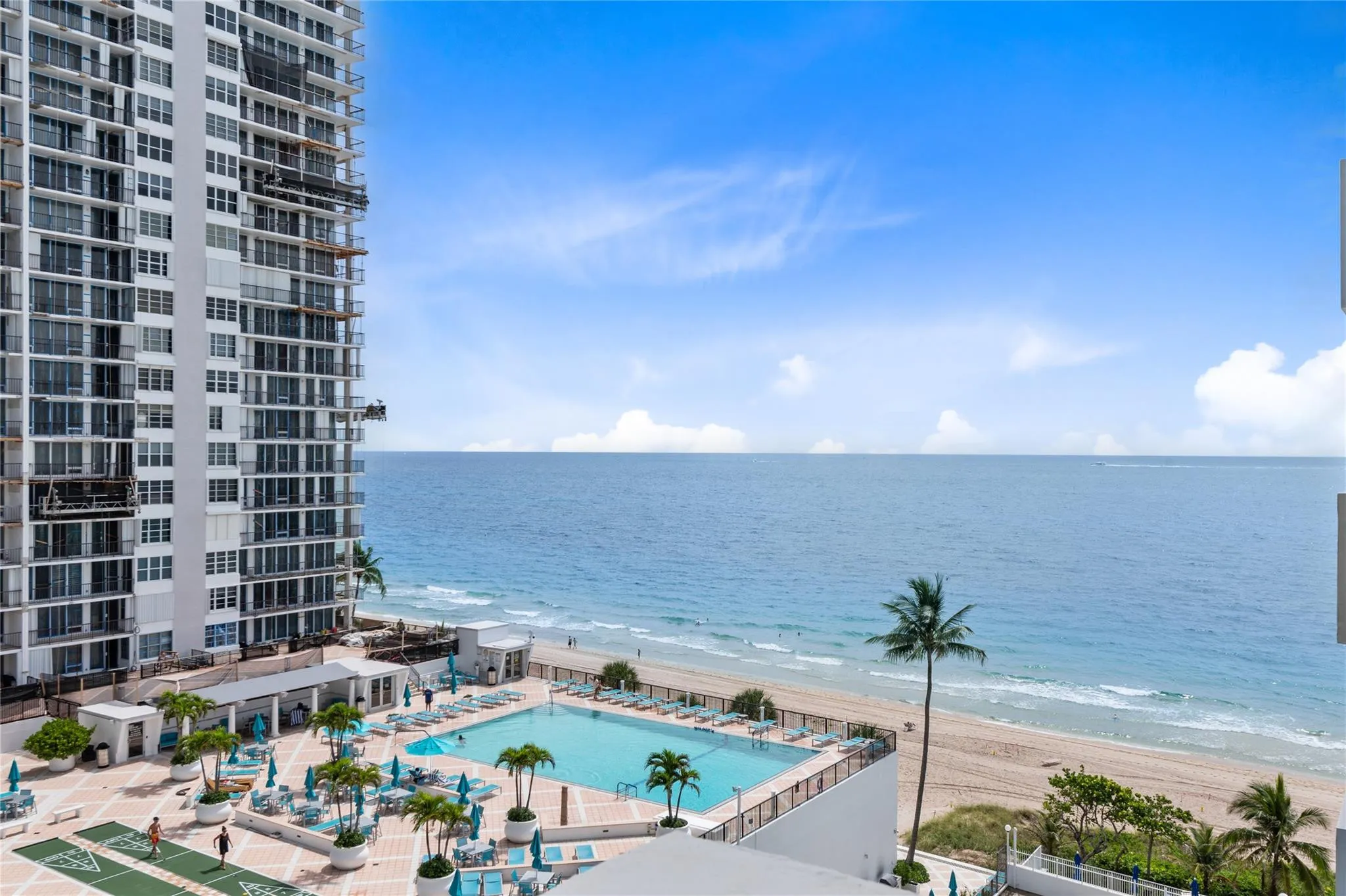 Expansive oceanfront setting featuring a resort-style pool, sandy beach, and tropical landscaping