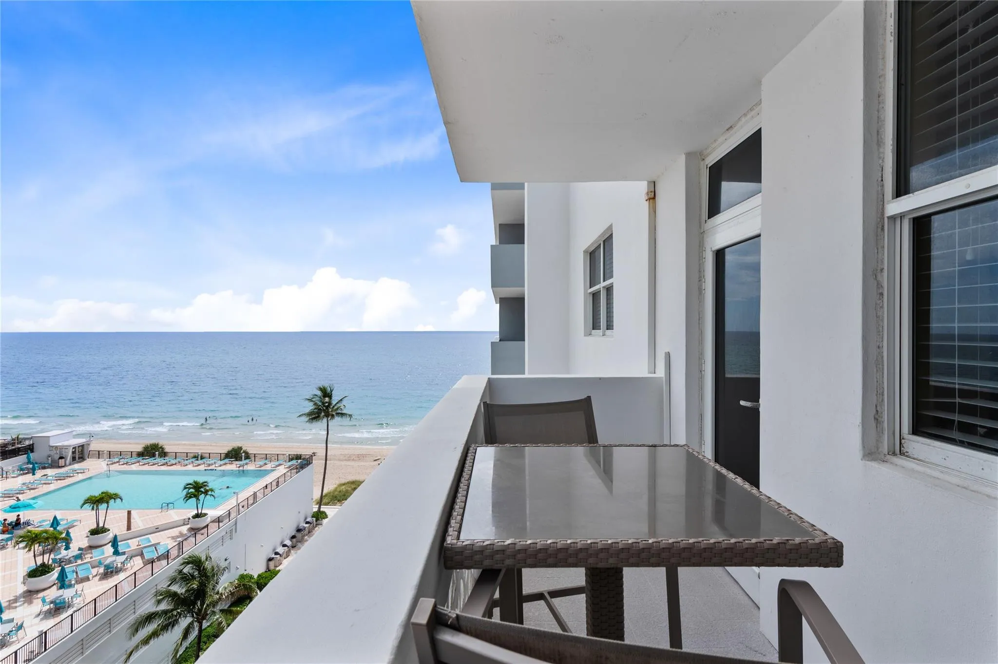 Private balcony with white railings, offering an oceanfront setting, and overlooking a resort-style pool