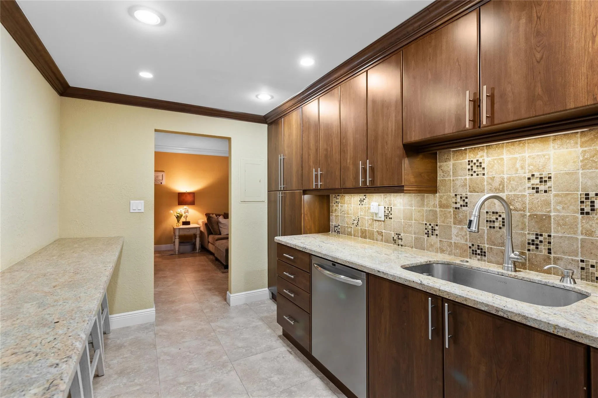 Kitchen featuring wood-finish cabinetry, granite countertops, a stainless steel sink, a tile backsplash with mosaic accents, and recessed lighting