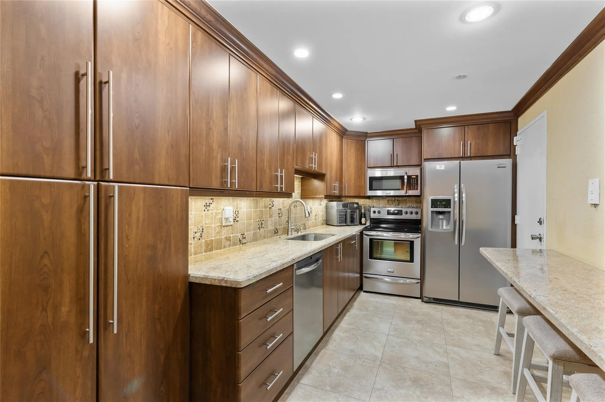 Kitchen featuring wood-finish cabinetry, stainless steel appliances, granite countertops, and a tiled backsplash