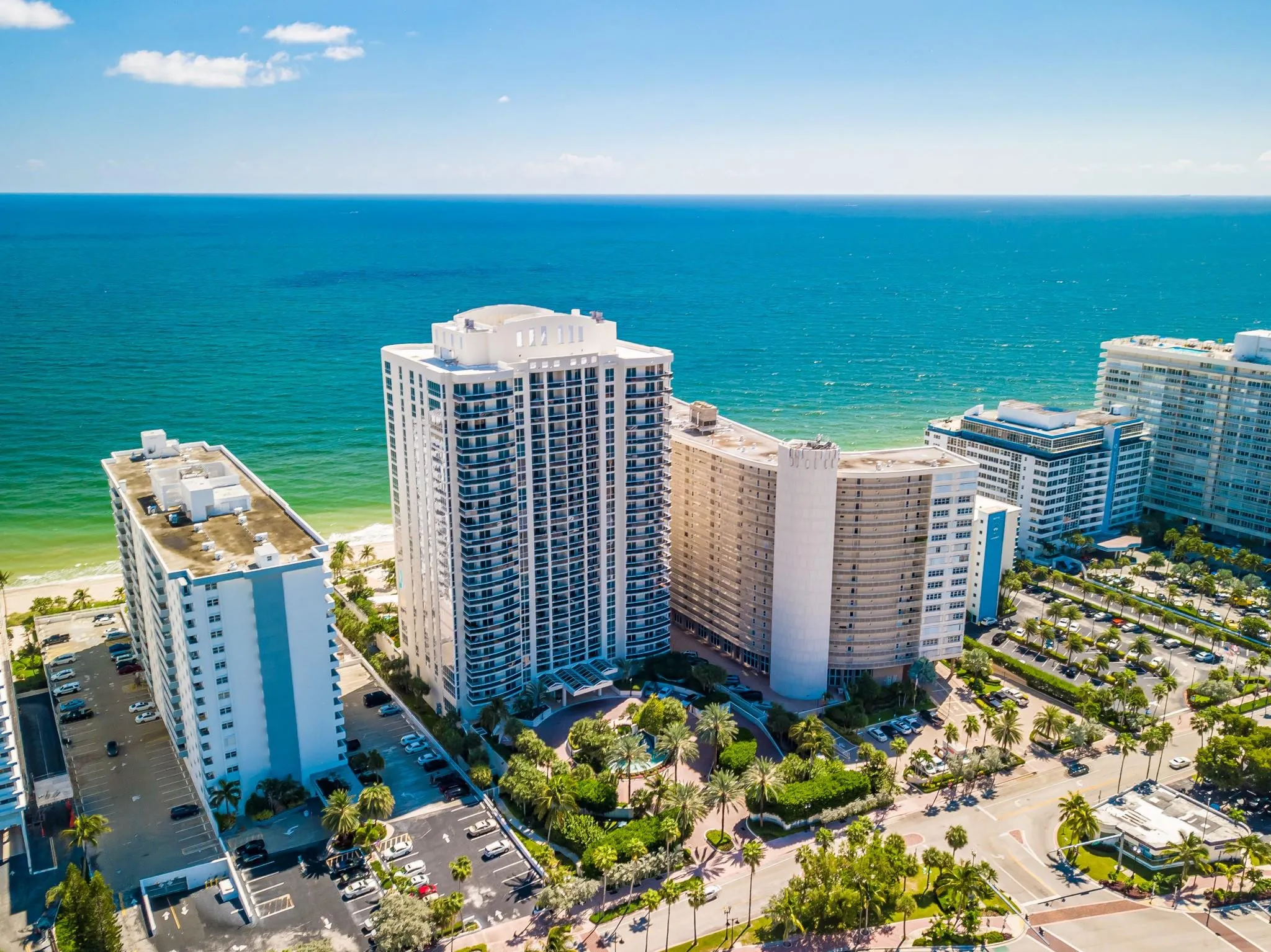 Coastal high-rise architecture with expansive ocean frontage, multiple parking areas, and mature landscaping