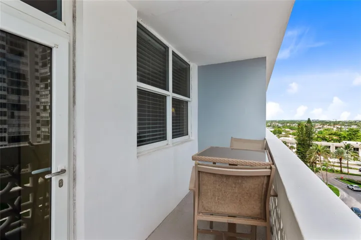 Balcony with partial glass entry door, white painted walls, and a patterned white railing