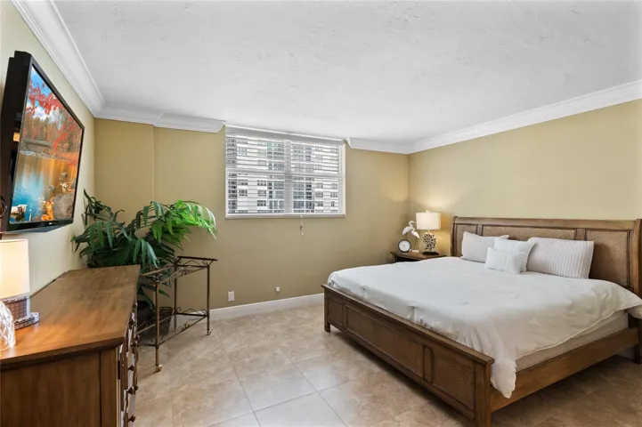 Recessed window with blinds, crown molding, wall-mounted television, and tile flooring