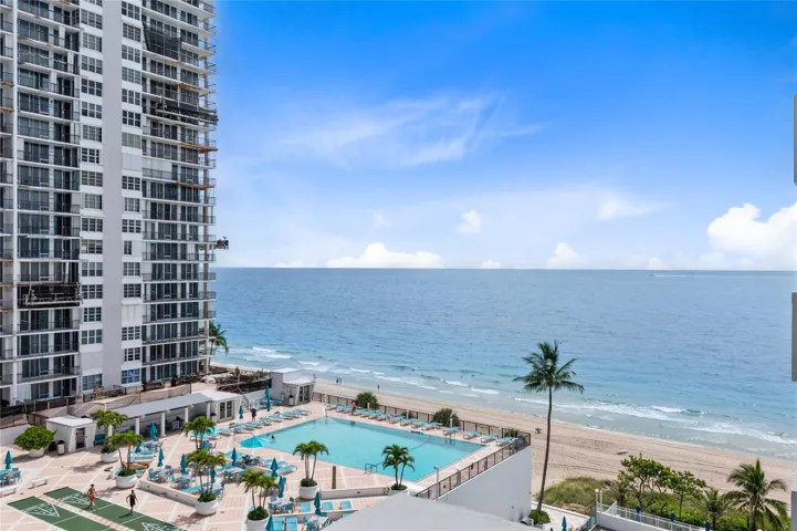 Expansive oceanfront setting featuring a resort-style pool, sandy beach, and tropical landscaping