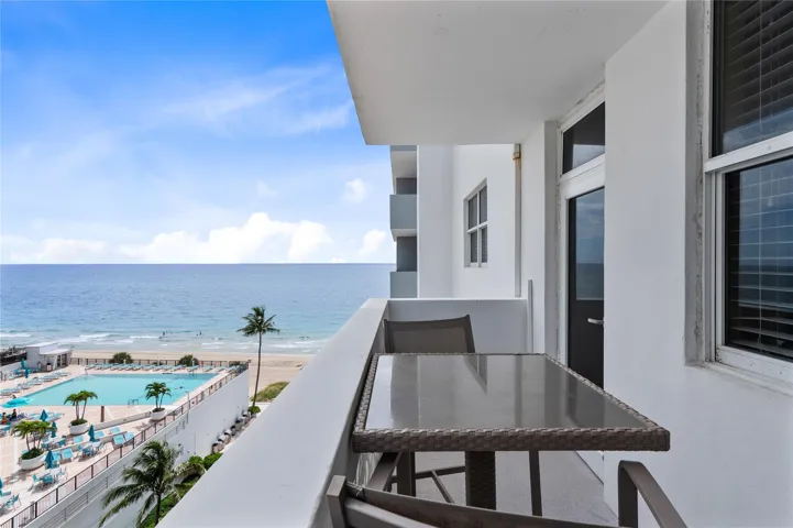 Private balcony with white railings, offering an oceanfront setting, and overlooking a resort-style pool