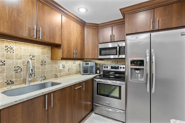 Full-height wood-finish cabinetry, stainless steel appliances, granite countertops, tile backsplash, and a contemporary gooseneck faucet